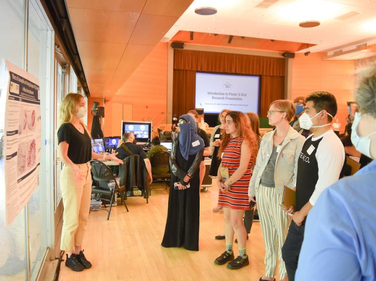 Student presenting their scientific poster to a crowd of student attendees at the 2022 SRA.