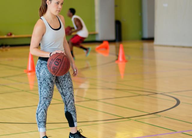 Woman dribbling basketball down court. 